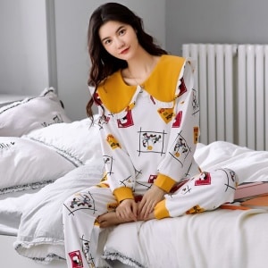 Högkvalitativ långärmad bomullspyjamas med manschetter för kvinnor som bärs av en kvinna som sitter på en säng i ett hus