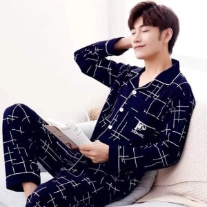 En man som sitter på en säng i ett hus bär en pyjamas i bomullsblå sommarblått
