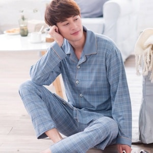 Trendig ljusblå bomullspyjamas för män som bärs av en man som sitter på en matta i ett hus
