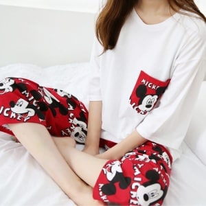 Röd och vit tvådelad pyjamas med Musse Pigg-motiv som bärs av en kvinna som sitter på en säng i mode