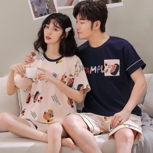 Tvådelad t-shirt och shorts i bomull med tecknat mönster som bärs av ett par som sitter i en soffa i ett hus