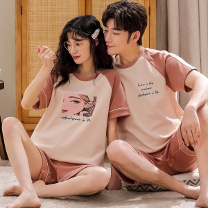 Tvådelad bomullspyjamas i en rosa vit t-shirt och rosa shorts som bärs av ett par som sitter på en matta i ett hus