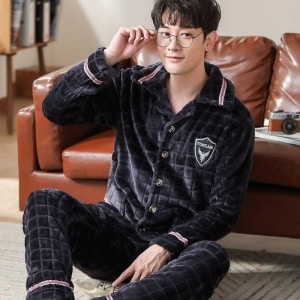 Flanellpyjamas för män med rutigt mönster som bärs av en man som sitter på en matta framför en soffa i ett hus