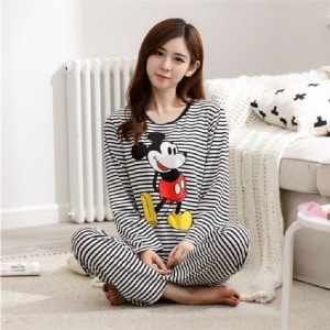 Randig Mickey-pyjamas för kvinnor som bärs av en kvinna som sitter framför en säng i ett hus