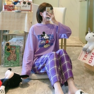 Musse Pigg-pyjamas med lila rutiga byxor som bärs av en kvinna som tar en bild i ett hus