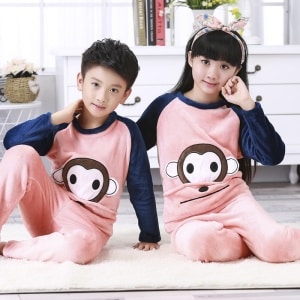 Pyjamas i flanell med aptryck för barn som bärs av en liten pojke och en liten flicka som sitter på en matta i ett hus