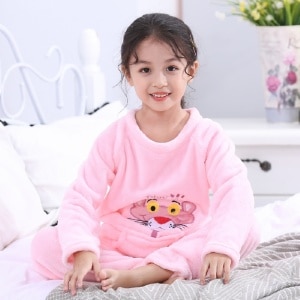 Flanellpyjamas i rosa panthertryck för en liten flicka som bärs på en säng i ett hus