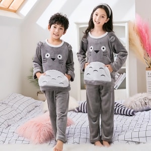 Pyjamas i grå fleece med Toroto-tryck för barn som bärs av en liten pojke och en liten flicka med pannband på en säng i ett hus