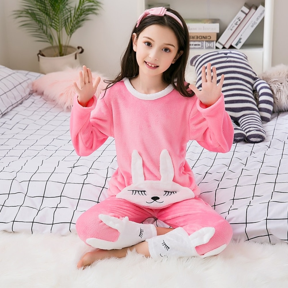 Rosa pyjamas i flanell med kaninmotiv för en flicka med pannband som sitter på en säng i ett hus