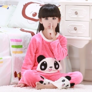 Rosa tvådelad pandapyjamas för en flicka som bärs av en liten flicka som sitter på en matta framför en säng i ett hus