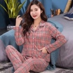 Moderiktig tvådelad dampyjamas i två delar med rutig krage som bärs av en kvinna som sitter på en matta framför en säng i ett hus