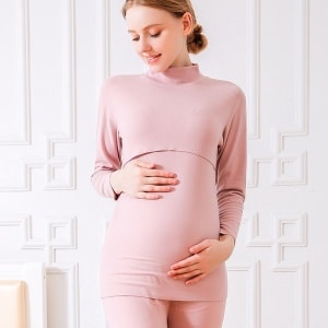 En gravid blond kvinna bär en rosa bomullspyjamas i två delar