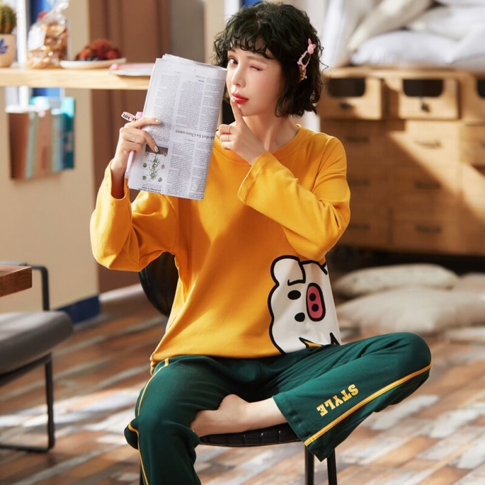 Bomullspyjamas med gul grisbyxor och gröna byxor som bärs av en kvinna som sitter på en stol och läser en tidning i ett hus