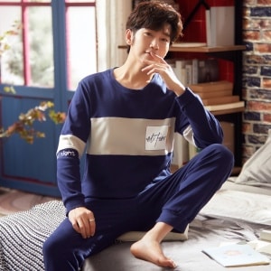 Marinblå bomullspyjamas i två delar med långa ärmar som bärs av en man som sitter på en säng i ett hus