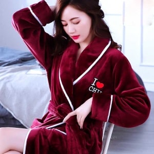 Pyjamas av röd korallfärgad fleece för kvinnor av mycket hög kvalitet som bärs av en kvinna som sitter på en stol i ett hus