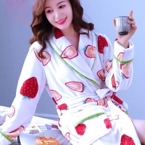 Moderiktig pyjamas i jordgubbsflickor för kvinnor, som bärs av en kvinna som sitter på en säng i ett hus