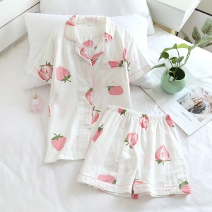 Kortärmad sommarpyjamas med jordgubbstryck för kvinnor på en säng med en liten vas och en blomma inuti i ett hus