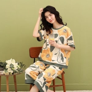 Tvådelad pyjamas för kvinnor med fladdermusärmar och modernt blommönster som bärs av en kvinna som sitter på en stol i ett hus