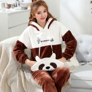 Tvådelad flanellpyjamas för kvinnor med pandamönster med en kvinna i pyjamas och en grå soffbakgrund med en vit filt