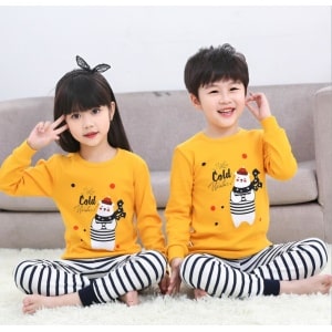Vårpyjamas med gul tröja och svartrandiga vita byxor med två barn i pyjamas och en soffa i bakgrunden