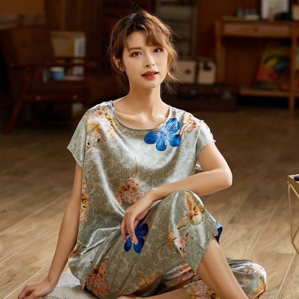 Tvådelad grå sommarpyjamas i siden satin med modernt blommönster som bärs av en kvinna som sitter på en matta i ett hus