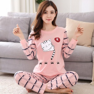 Söt tvådelad långärmad pyjamas för kvinnor som bärs av en kvinna som sitter på en matta framför en stol i ett hus