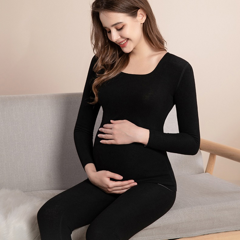 ung gravid kvinna som sitter i svart pyjamas och ler när hon rör vid sin runda mage