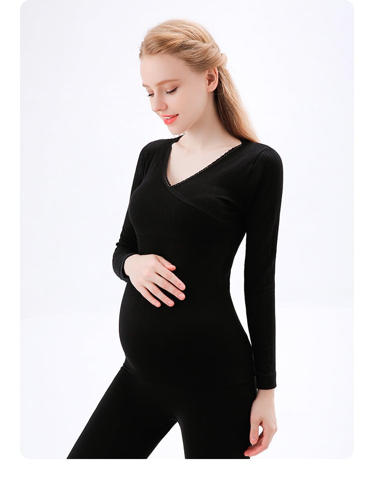 gravid kvinna som rör vid sin mage med en hand, klädd i en svart pyjamas bestående av byxor och en långärmad tröja