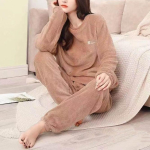 ung kvinna i beige pilou pilou pyjamas, hon sitter på en ruta nära en soffa, på golvet, hakan vilar i en av hennes händer