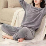 ung kvinna i grå pilou pilou pyjamas, hon sitter på en plaid bredvid en soffa, på golvet, med händerna korsade bakom huvudet