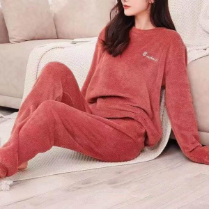 ung kvinna i röd pilou pilou pyjamas, hon sitter på en plaid bredvid en soffa på golvet